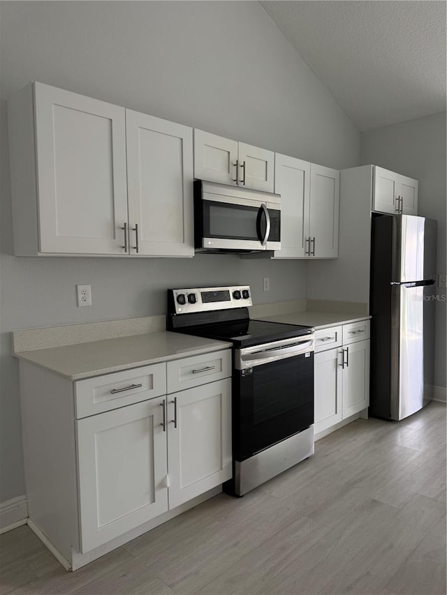 kitchen featuring light wood finished floors, white cabinets, vaulted ceiling, stainless steel appliances, and light countertops