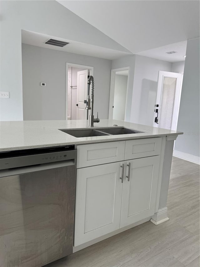 kitchen with white cabinets, dishwasher, light stone counters, light wood-type flooring, and a sink