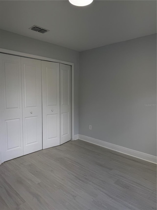 unfurnished bedroom with baseboards, a closet, visible vents, and wood finished floors