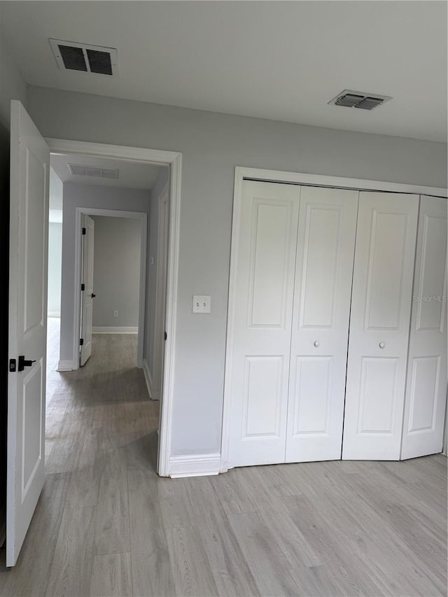 unfurnished bedroom featuring baseboards, a closet, visible vents, and light wood-style floors