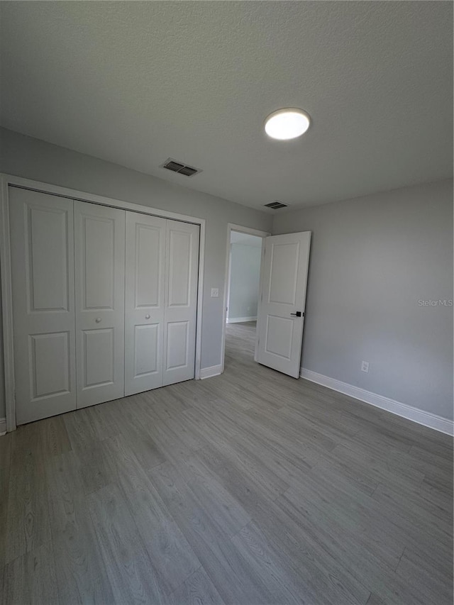 unfurnished bedroom with a closet, visible vents, a textured ceiling, wood finished floors, and baseboards