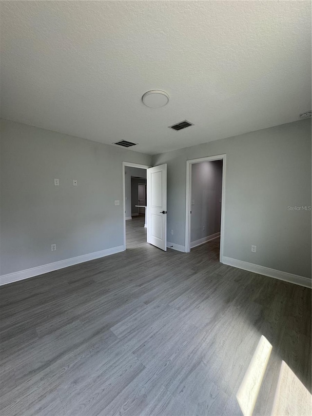 unfurnished room featuring a textured ceiling, dark wood-style flooring, visible vents, and baseboards