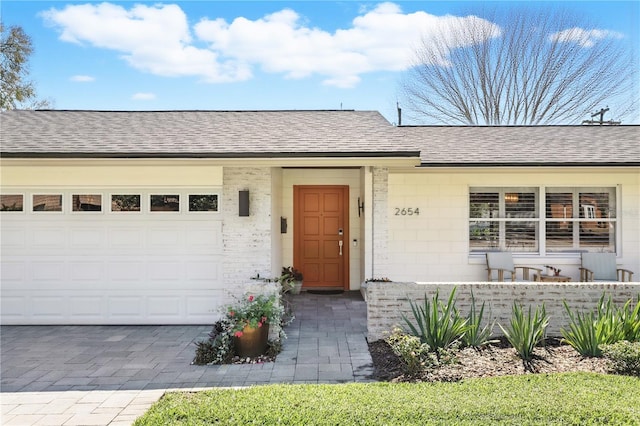 property entrance with decorative driveway, roof with shingles, and an attached garage