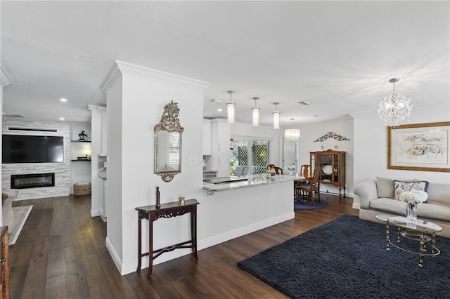 living area with dark wood-style floors, a large fireplace, ornamental molding, and an inviting chandelier