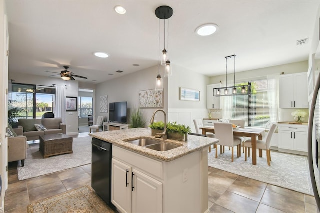 kitchen featuring light stone counters, black dishwasher, hanging light fixtures, a kitchen island with sink, and a sink