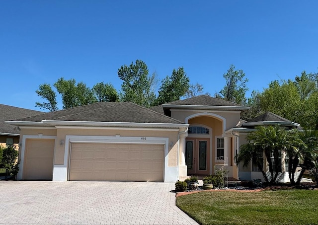 view of front of house with decorative driveway, an attached garage, and stucco siding