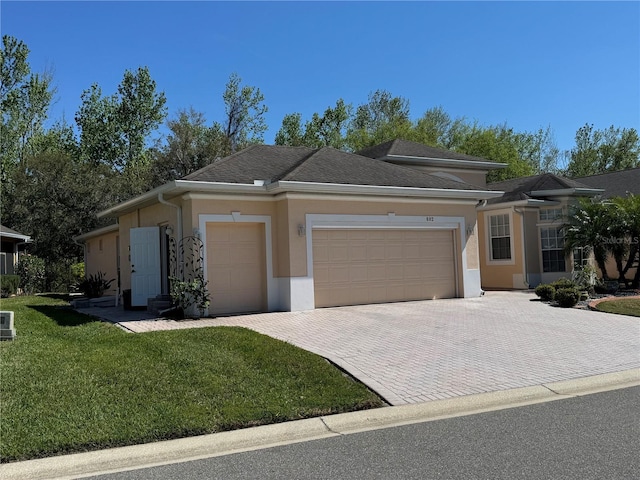 prairie-style house featuring an attached garage, roof with shingles, decorative driveway, stucco siding, and a front lawn