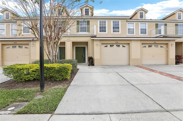 townhome / multi-family property with driveway, a balcony, an attached garage, and stucco siding