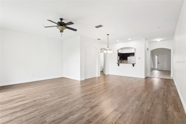 unfurnished living room with baseboards, visible vents, arched walkways, wood finished floors, and ceiling fan with notable chandelier