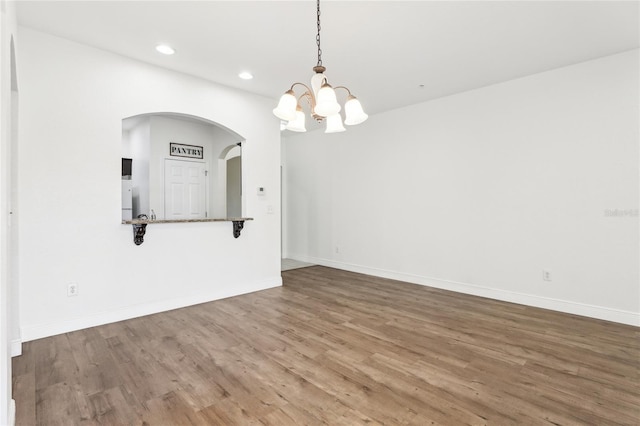 spare room featuring recessed lighting, an inviting chandelier, baseboards, and wood finished floors