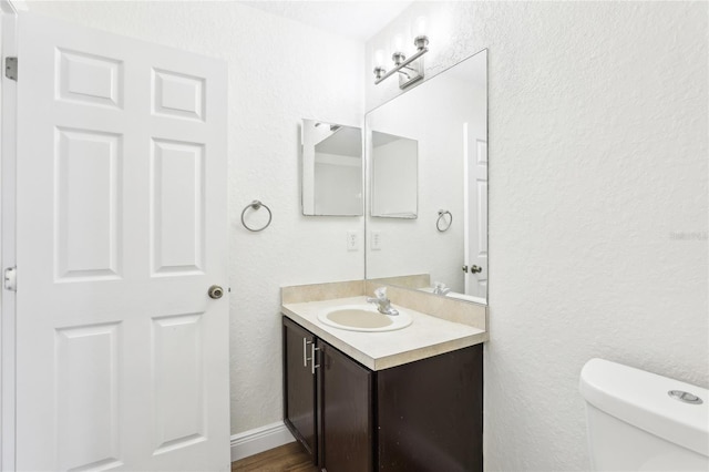 half bathroom with toilet, a textured wall, wood finished floors, and vanity