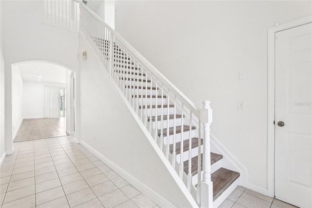 stairway with arched walkways, tile patterned flooring, a towering ceiling, and baseboards