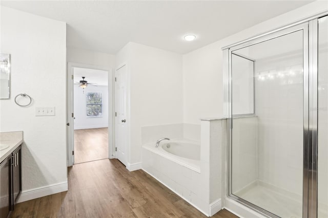 full bath with wood finished floors, vanity, baseboards, a bath, and a stall shower