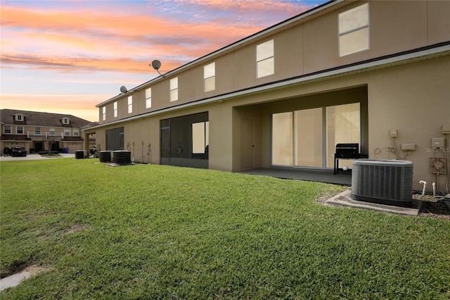 back of property at dusk featuring central AC unit, a lawn, and stucco siding