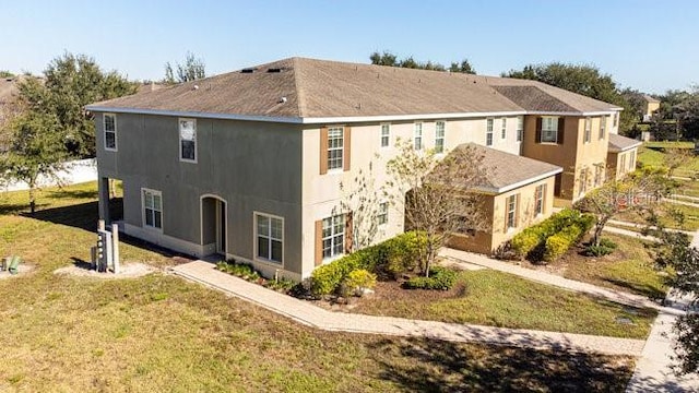 rear view of property featuring a lawn and stucco siding