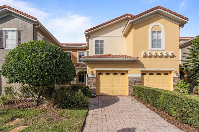 mediterranean / spanish-style house featuring decorative driveway, stone siding, a tile roof, and stucco siding