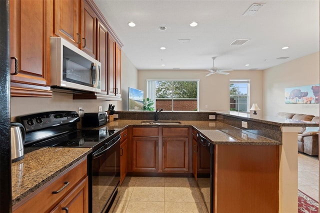 kitchen with visible vents, dark stone counters, a peninsula, black appliances, and a sink