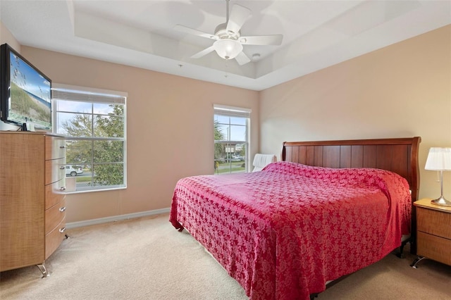 bedroom with light carpet, ceiling fan, a raised ceiling, and baseboards