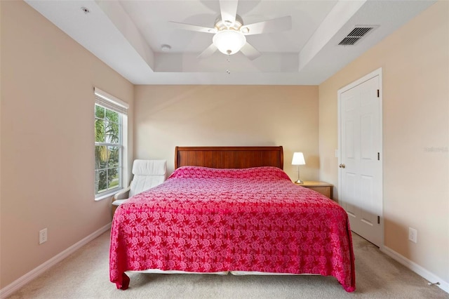 bedroom with a tray ceiling, visible vents, light carpet, and baseboards