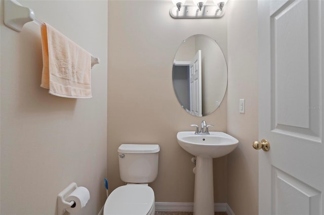 half bath featuring toilet, baseboards, and a sink