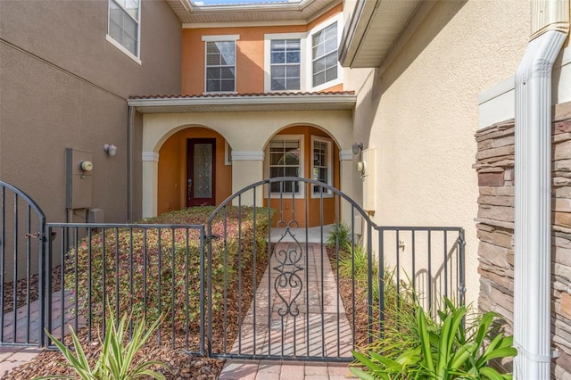 view of exterior entry with a gate, fence, and stucco siding