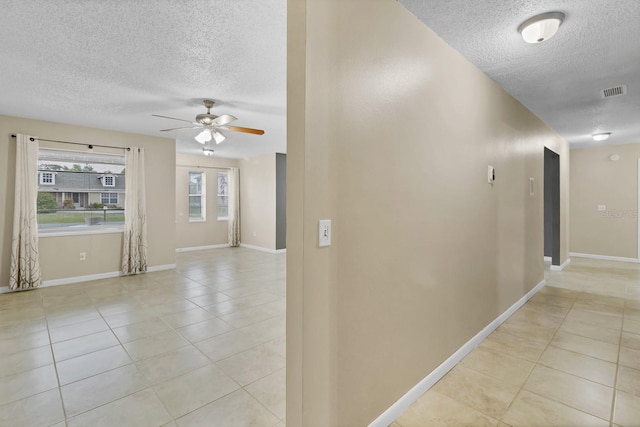 hallway with light tile patterned floors, baseboards, visible vents, and a textured ceiling