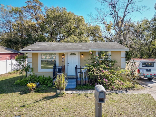 view of front of property with fence, a front lawn, and stucco siding