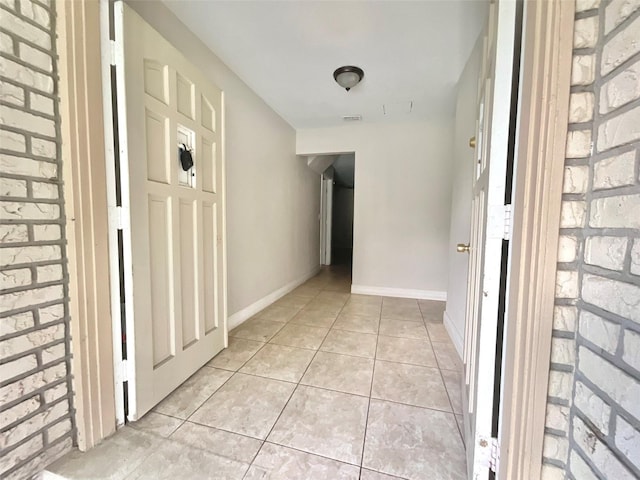 corridor featuring brick wall, visible vents, baseboards, and light tile patterned floors