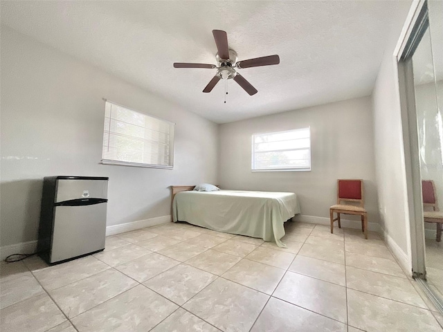 bedroom with light tile patterned floors, ceiling fan, baseboards, and a textured ceiling