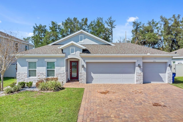 single story home with an attached garage, stone siding, decorative driveway, stucco siding, and a front lawn