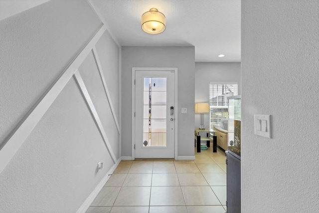 foyer with light tile patterned flooring, a textured wall, and baseboards