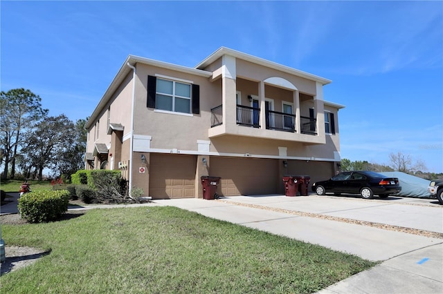 view of front facade with an attached garage, a balcony, concrete driveway, stucco siding, and a front lawn