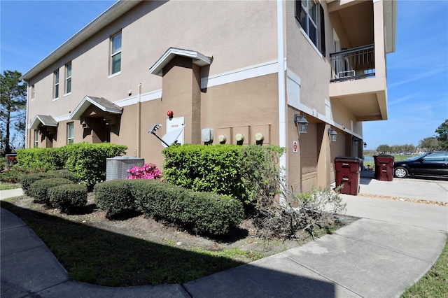 view of side of property featuring driveway, central AC, an attached garage, and stucco siding