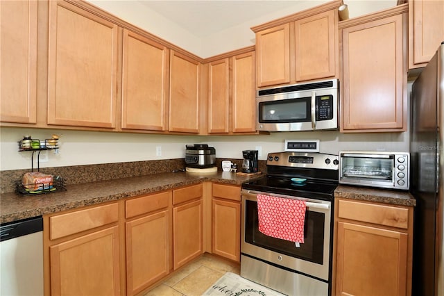 kitchen featuring dark countertops, light tile patterned floors, light brown cabinets, and appliances with stainless steel finishes