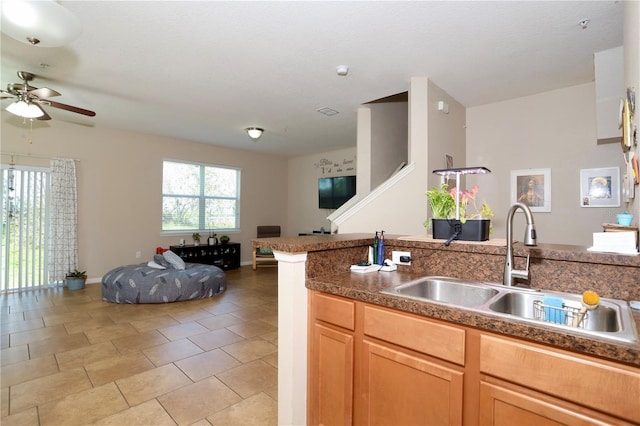 kitchen with light tile patterned floors, a sink, a ceiling fan, baseboards, and open floor plan