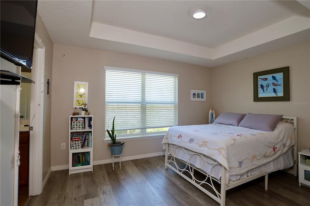 bedroom featuring a tray ceiling, wood finished floors, and baseboards