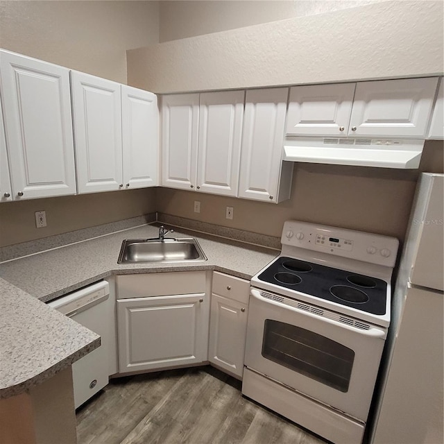 kitchen featuring white appliances, wood finished floors, under cabinet range hood, white cabinetry, and a sink