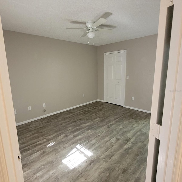 empty room featuring a ceiling fan, dark wood-style flooring, a textured ceiling, and baseboards