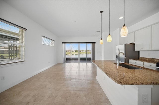 kitchen featuring dark stone counters, open floor plan, white cabinetry, stainless steel refrigerator with ice dispenser, and a sink