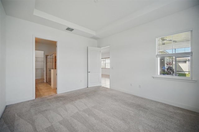 unfurnished bedroom with baseboards, carpet, visible vents, and a tray ceiling