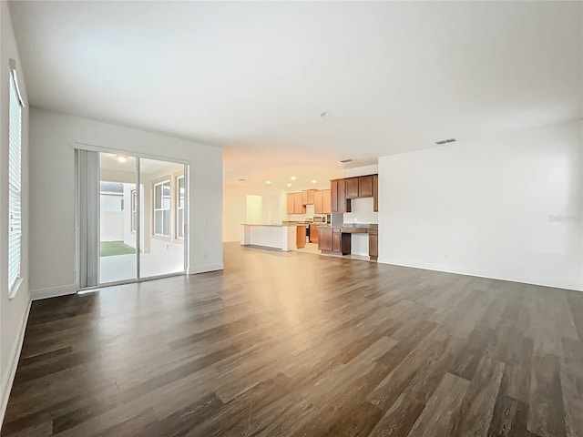 unfurnished living room with baseboards, visible vents, and dark wood-style flooring