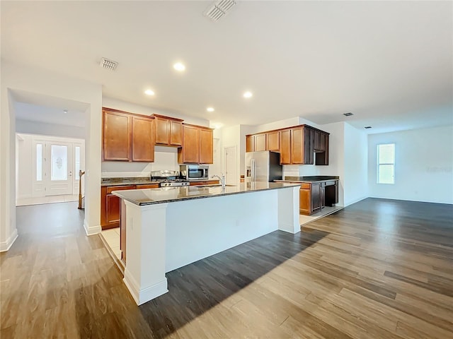 kitchen with stainless steel appliances, an island with sink, wood finished floors, and visible vents