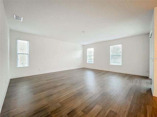 spare room featuring dark wood-style flooring, visible vents, and baseboards