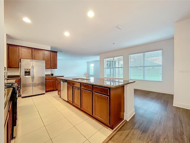 kitchen featuring light stone counters, visible vents, appliances with stainless steel finishes, a sink, and an island with sink