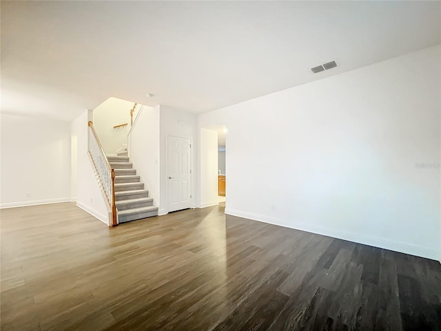 unfurnished living room featuring dark wood-style flooring, visible vents, baseboards, and stairs