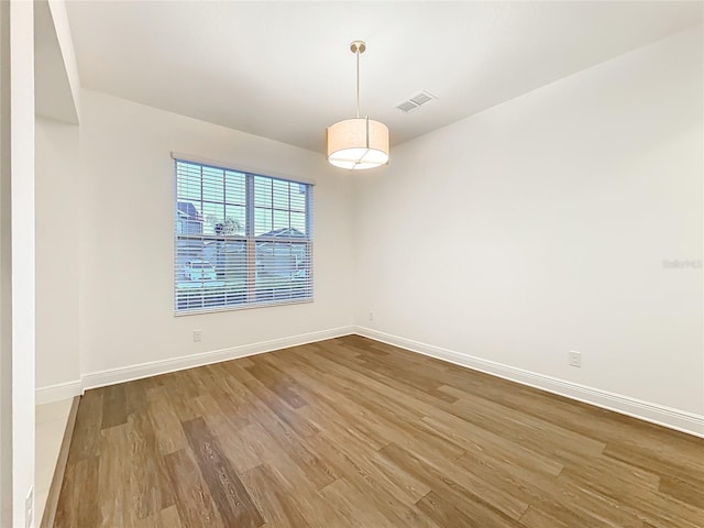 spare room featuring wood finished floors, visible vents, and baseboards