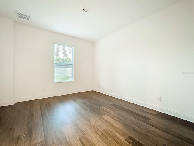 unfurnished room featuring dark wood-style floors, visible vents, and baseboards