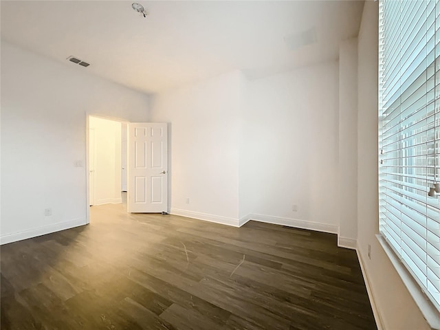 spare room with dark wood-type flooring, visible vents, and baseboards