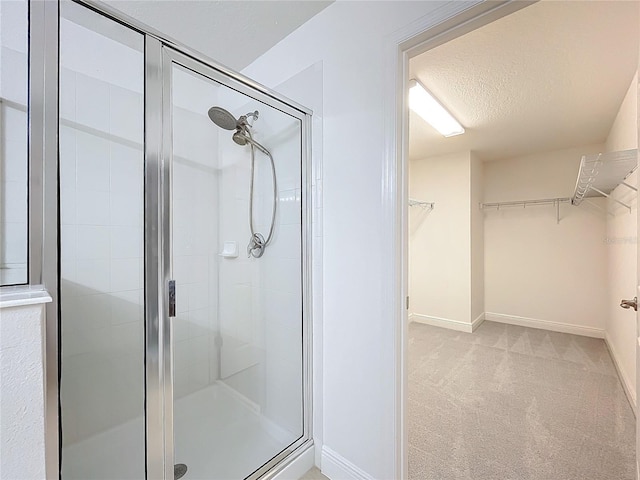 full bath with a textured ceiling, a stall shower, a walk in closet, and baseboards