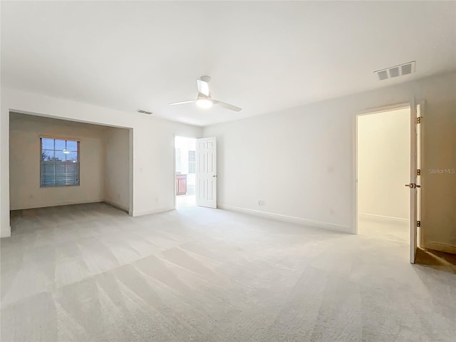 empty room featuring a ceiling fan, visible vents, light carpet, and baseboards